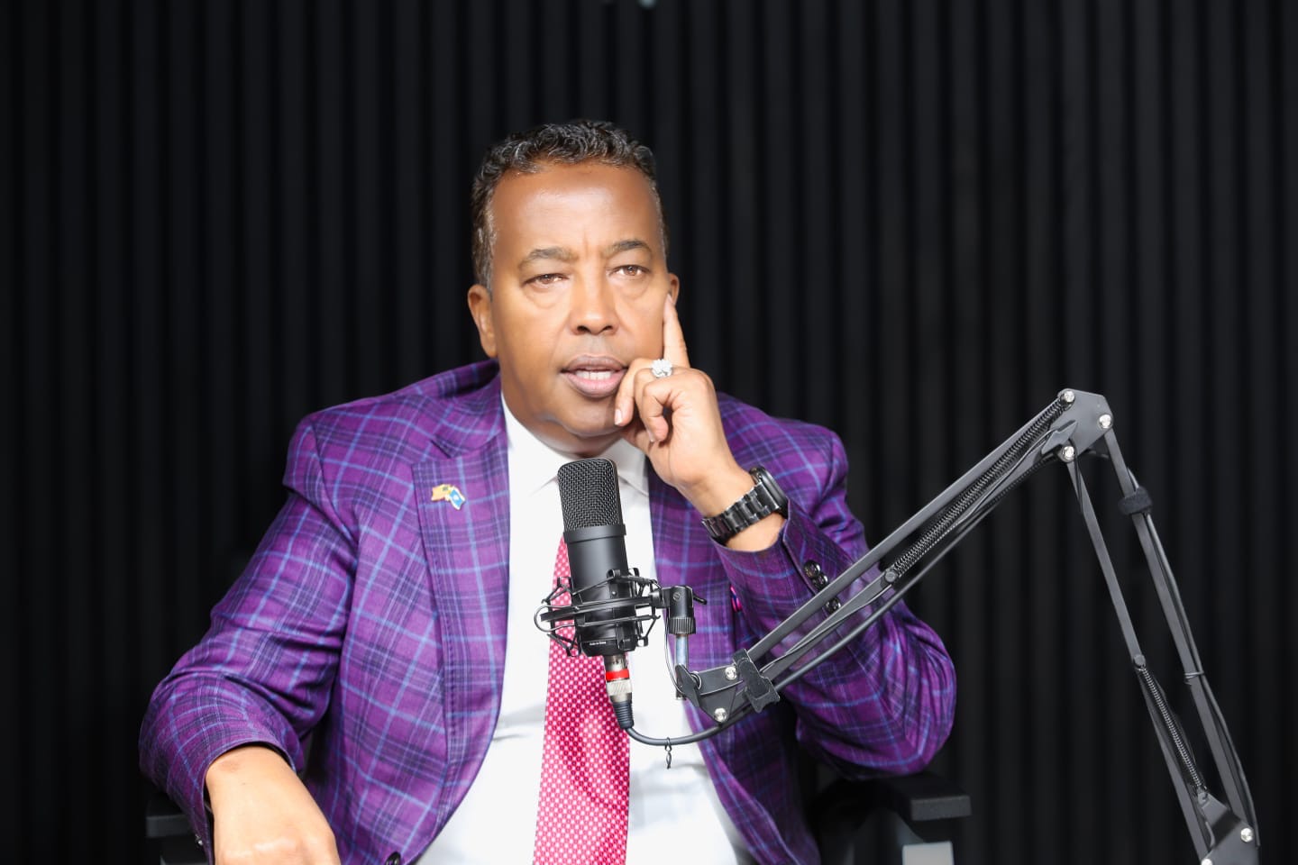 Istoosi Media host wearing a purple suit at a podcast microphone