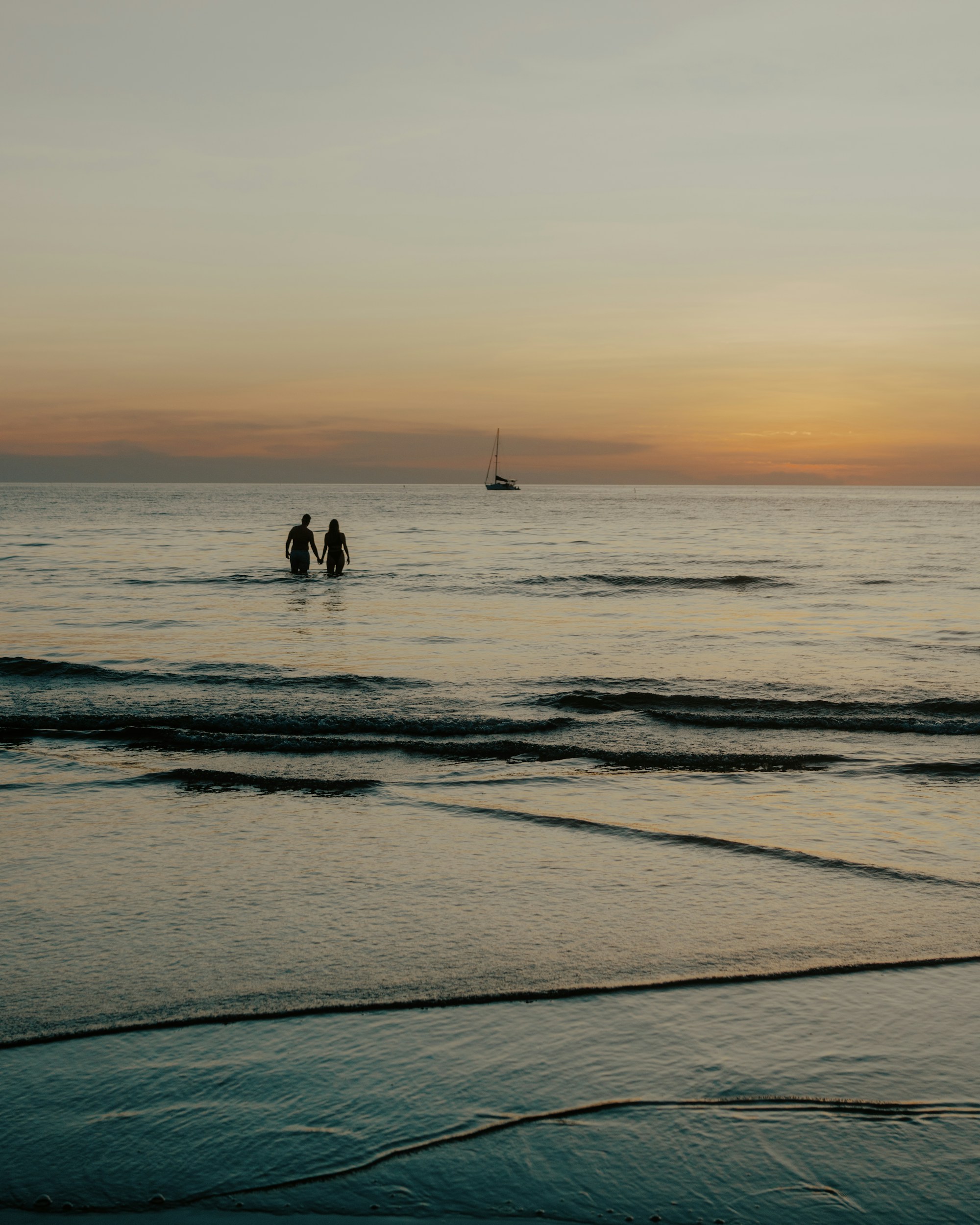 A couple holding hands in the ocean at sunset